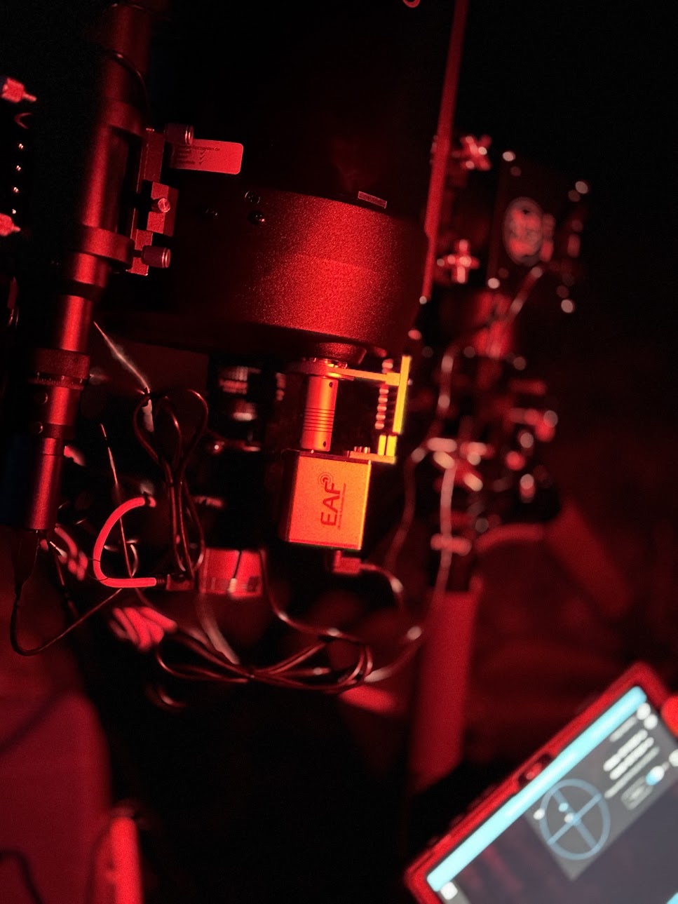Nahaufnahme eines Astro-Setups mit Fokussiermotor im Rotlicht, daneben ein Tablet mit Steuerungssoftware