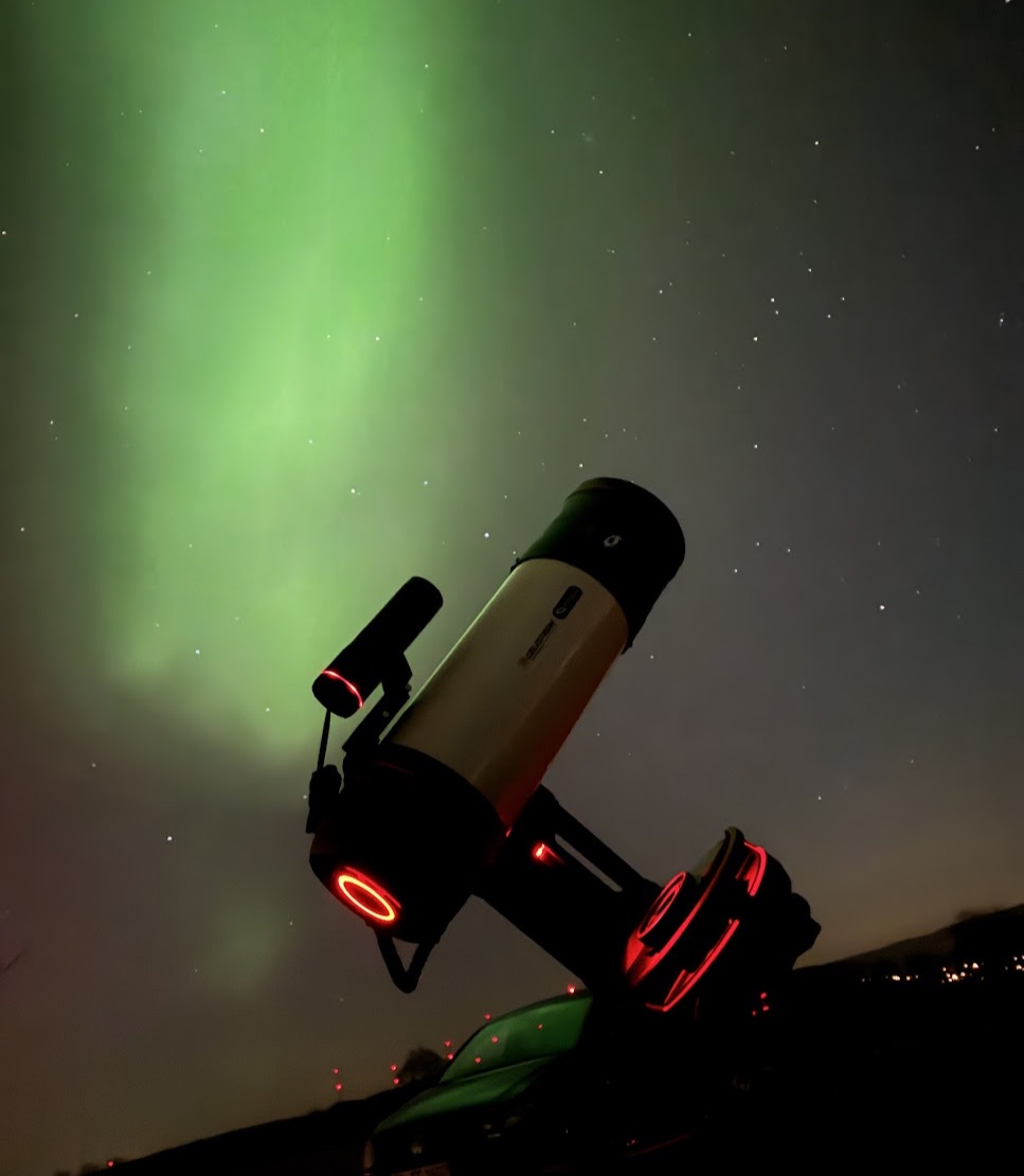 Teleskop auf Montierung vor grünem Polarlicht